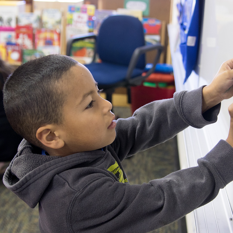 young boy placing magnet on classroom whiteboard