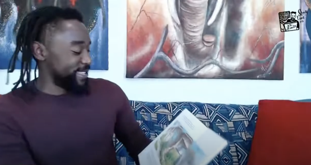 Image of a Black male teacher sitting on a couch reading a children's picture book